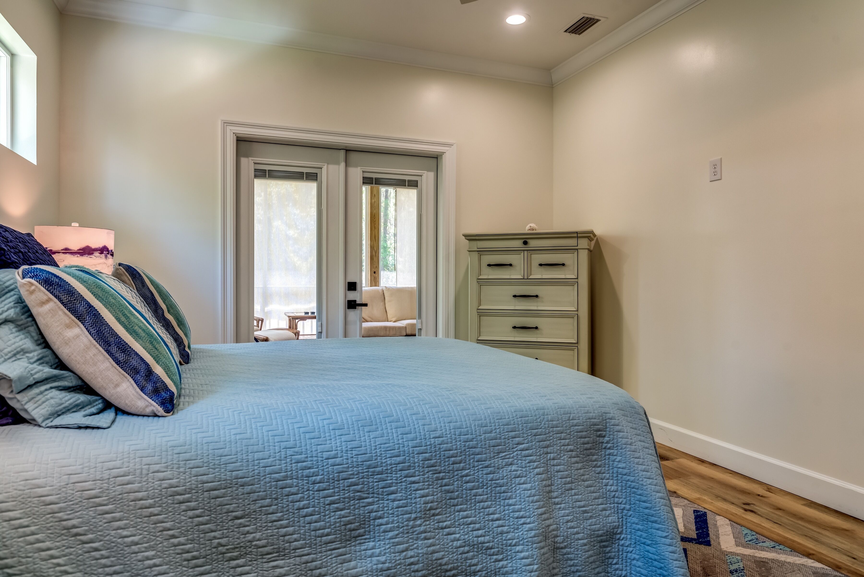 A bedroom with a bed, a dresser, and a door leading to a balcony.
