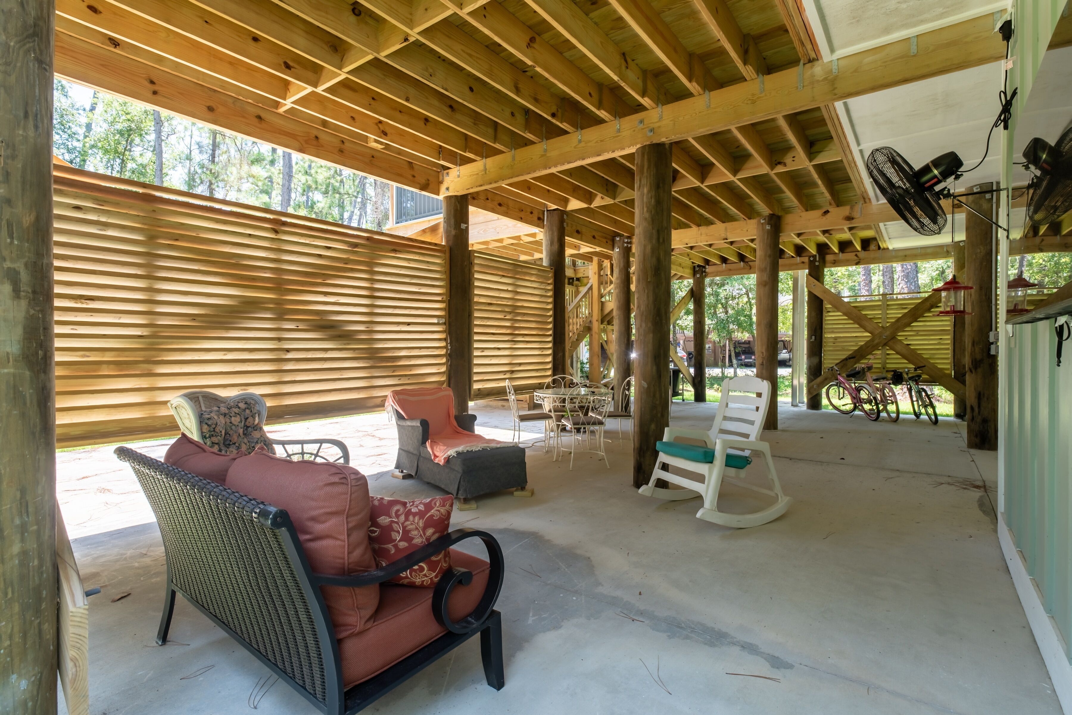 An outdoor covered patio with wooden beams, wicker furniture, and a bicycle.