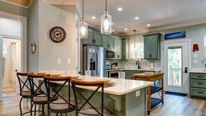 A modern kitchen with a central island, bar stools, and pendant lighting.