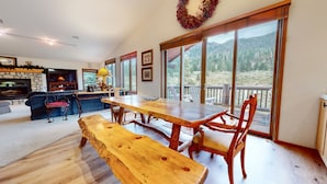 A spacious living area with a wooden dining table, benches, and a large window offering a view of a forested landscape.