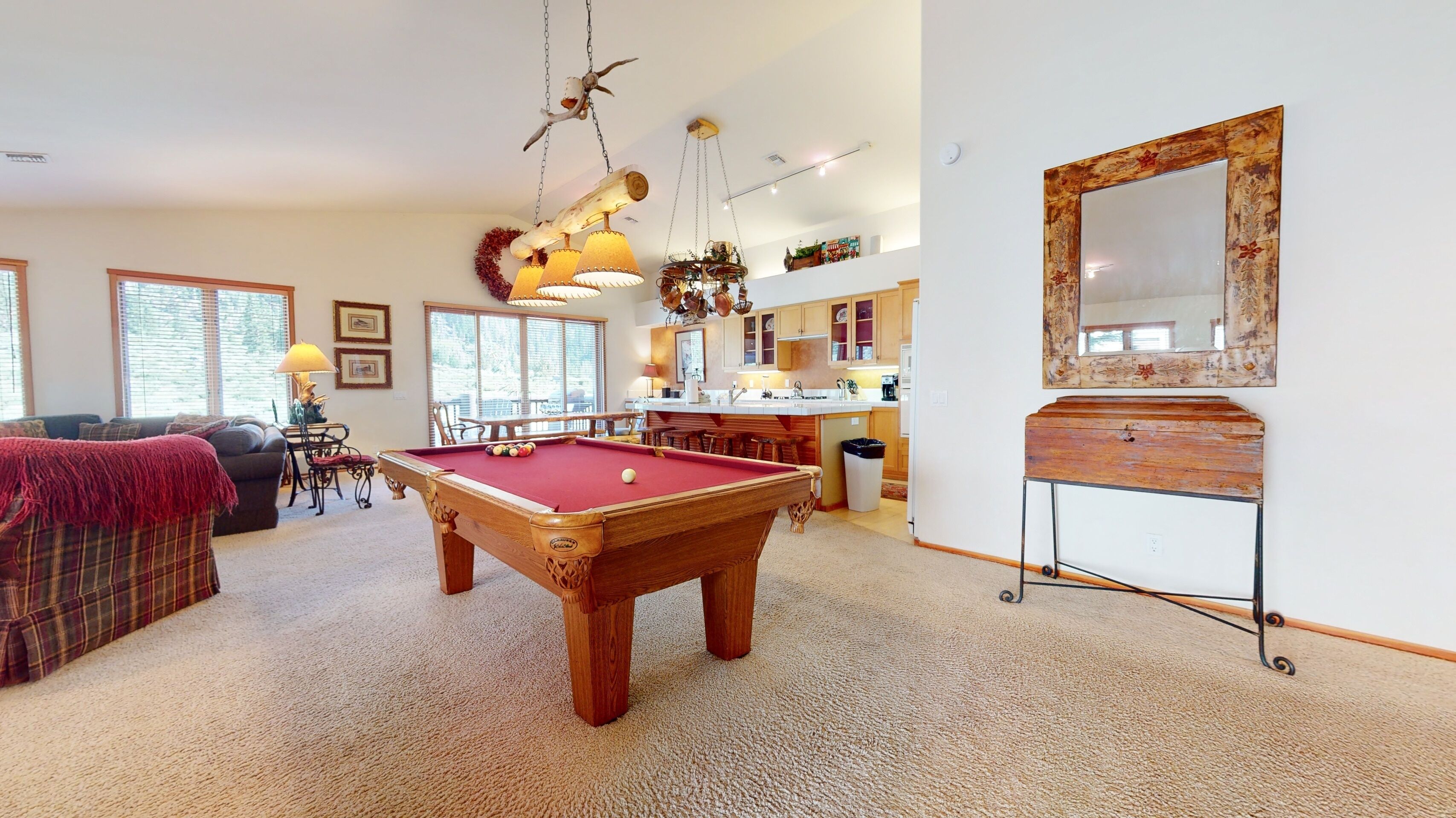 Un vaste salon comprenant une table de billard, un coin salon confortable et une cuisine dotée de meubles en bois.