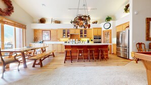 A spacious kitchen with wooden cabinetry, a central island with stools, a large refrigerator, and a hanging light fixture.