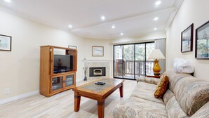 Un salon comprenant un meuble de rangement en bois pour les appareils multimédias, une cheminée, un canapé et une grande fenêtre offrant une vue dégagée.