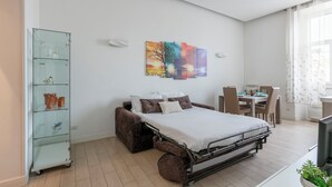 A compact bedroom with a bed, a glass cabinet with items, a painting, and a dining area. - Manzoni Apartment (Roma)