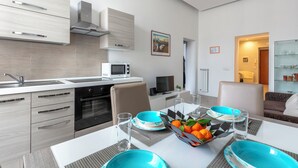 A modern kitchen with a microwave, oven, and stainless steel appliances. There is a dining area with a table set for two, featuring blue and white plates and a fruit bowl. - Manzoni Apartment (Roma)