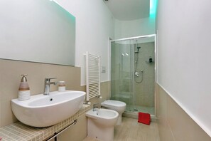 Moderni kylpyhuone, jossa on suuri pesuallas, wc ja lasiseinällä varustettu suihku.