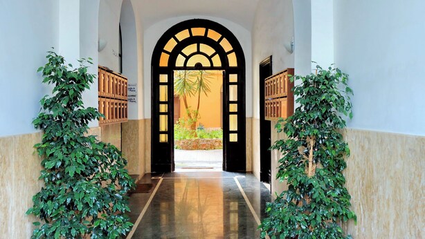 A hallway with a marble floor, an arched doorway, and potted plants on either side. - Manzoni Apartment (Roma)