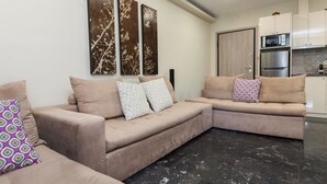 A modern living room with a beige sectional sofa, a coffee table, and a kitchen area with white cabinets and stainless steel appliances. - Stylish Athinas House in Kallithea (Kallithea)