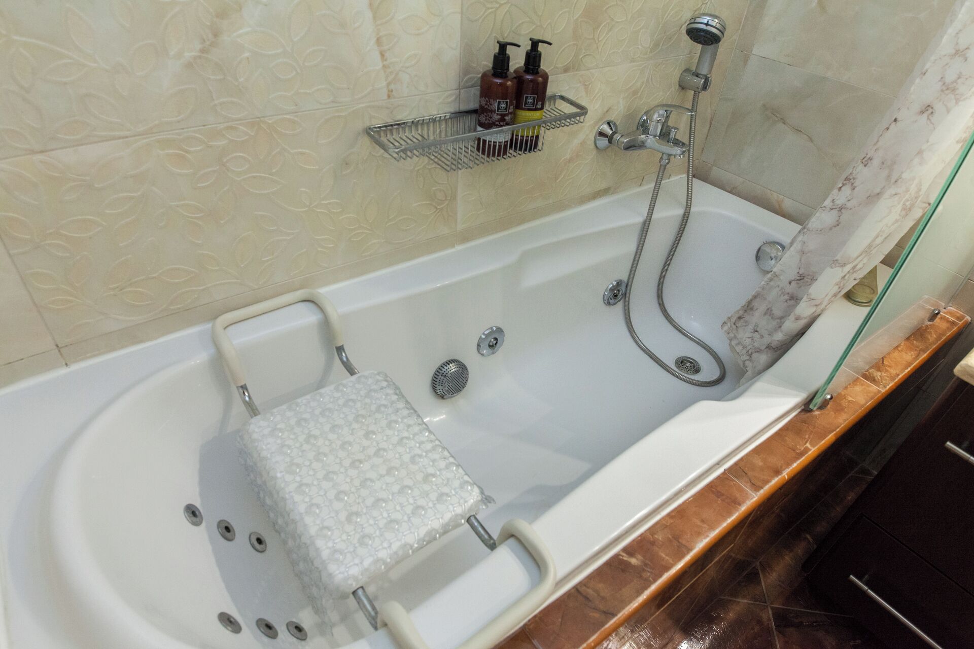 Eine Badewanne mit integriertem Sitz, einer Handbrause und einem Seifenspender auf einem Regal darüber.