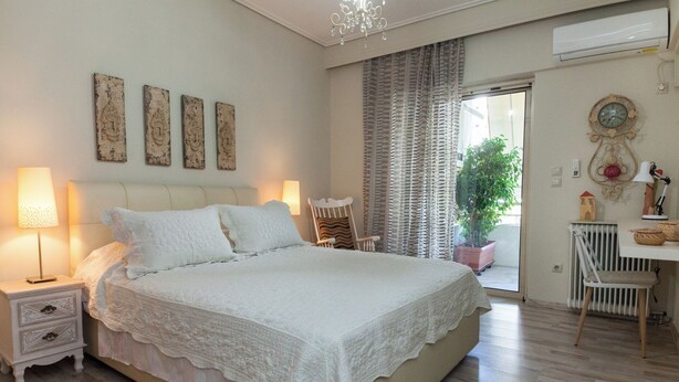 A bedroom with a large bed, two bedside tables with lamps, a chair, a potted plant, and a desk with a lamp. - Stylish Athinas House in Kallithea (Kallithea)