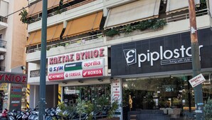 A multi-story building with various storefronts, including a visible sign for 'KOSTA BYNIOΣ' and 'epiplostar'. - Stylish Athinas House in Kallithea (Kallithea)