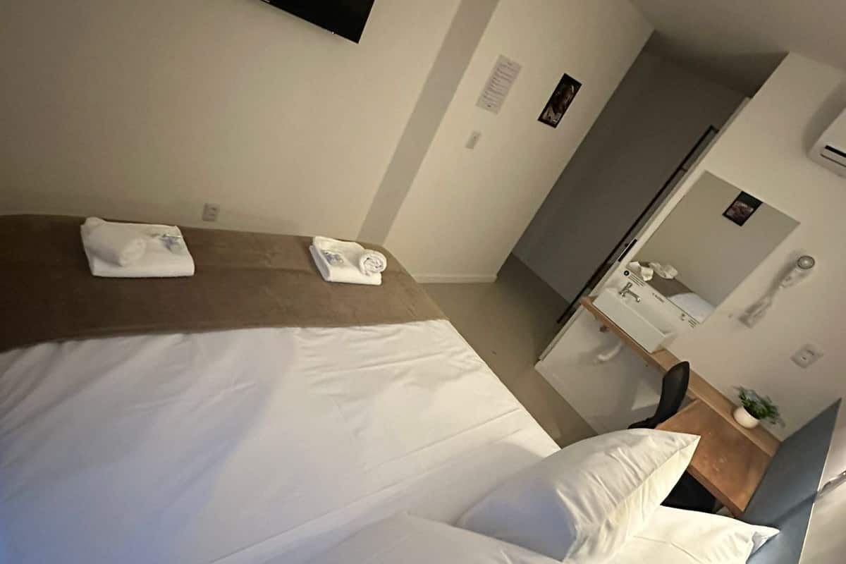 A hotel room with a bed, a TV mounted on the wall, a bathroom with a mirror, and a small table with a plant.