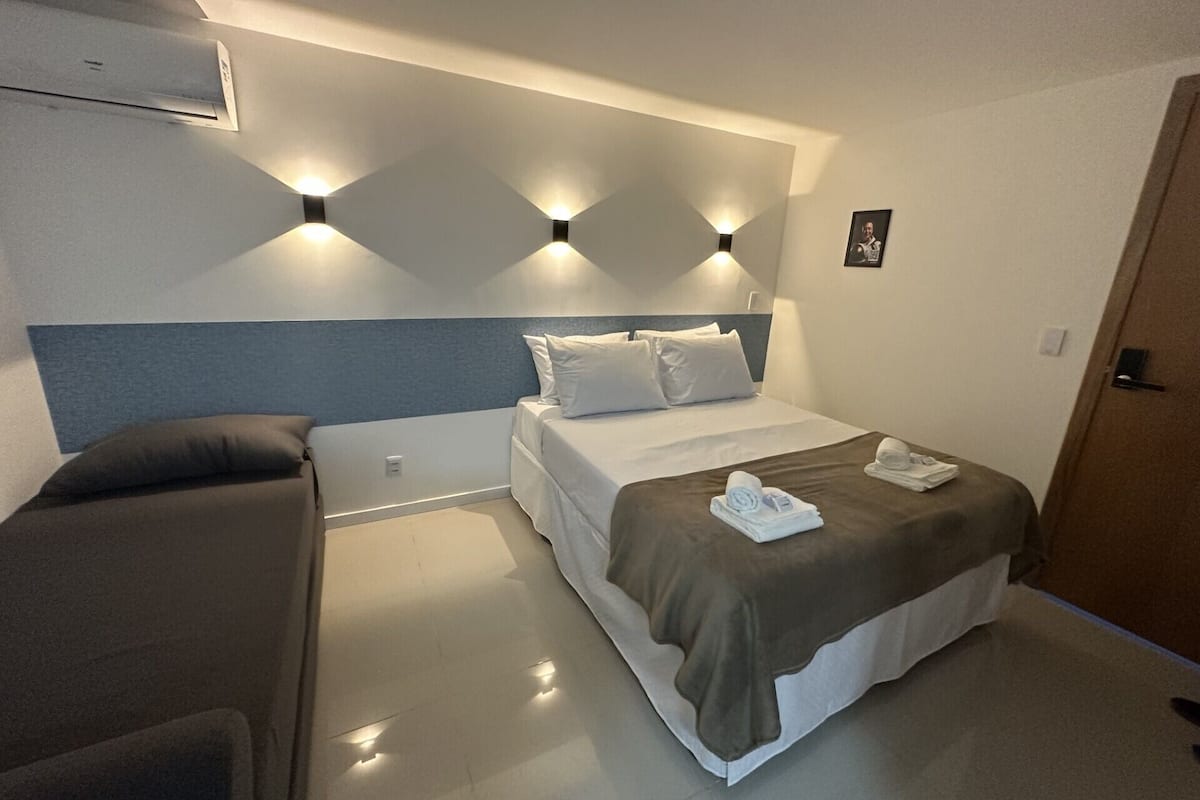 A hotel room with a bed, a sofa, and a wall-mounted air conditioner.