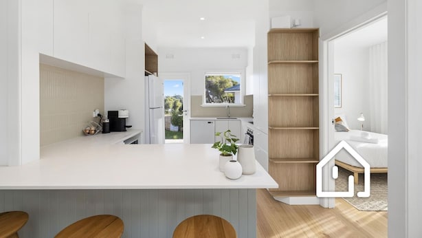 Une cuisine moderne avec un îlot central, des étagères en bois et une vue sur le jardin arrière.