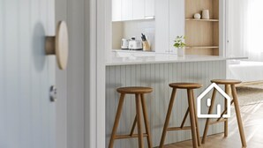 Une cuisine moderne avec des meubles blancs, des tabourets en bois et une petite plante en pot.