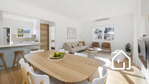 Un espace de vie moderne et ouvert, comprenant une table à manger centrale, un ensemble de canapés et un coin cuisine.