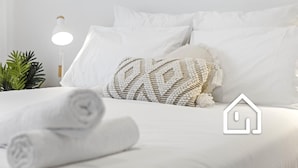 Un lit bien fait, avec des draps blancs, un coussin décoratif et une lampe de chevet.