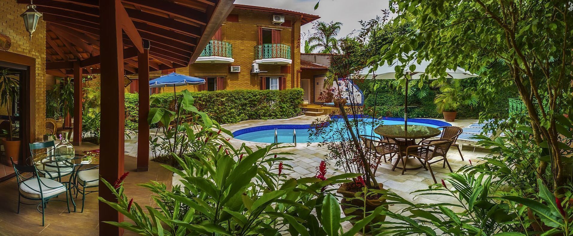 Zona de piscina con una pileta circular, rodeada de abundante vegetación y mobiliario exterior.