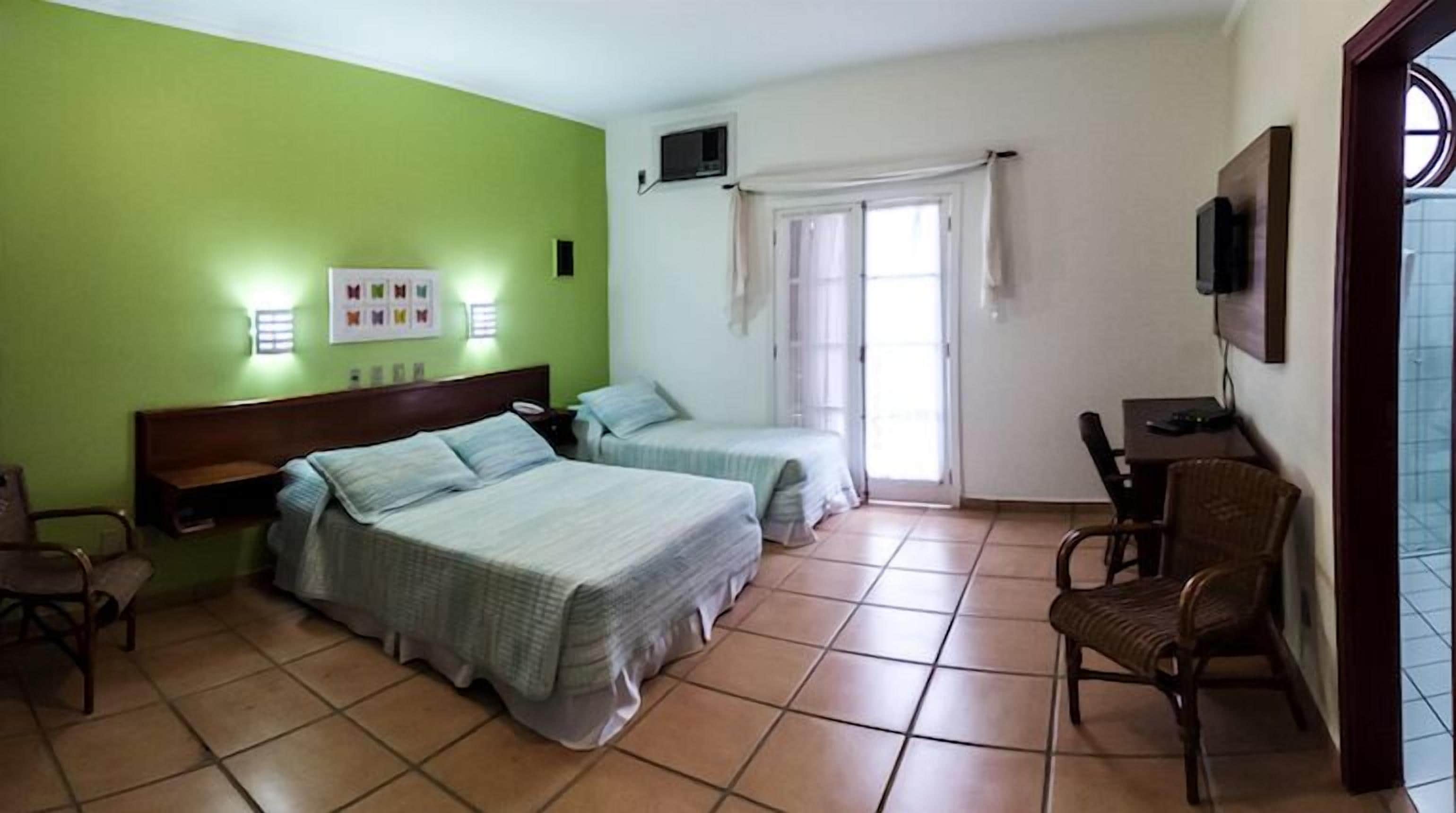 A hotel room with two beds, a desk, a chair, a TV, and a window with curtains.