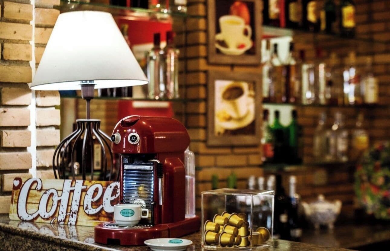 Uma máquina de café, uma lâmpada e um recipiente de vidro com cápsulas de café em uma bancada.