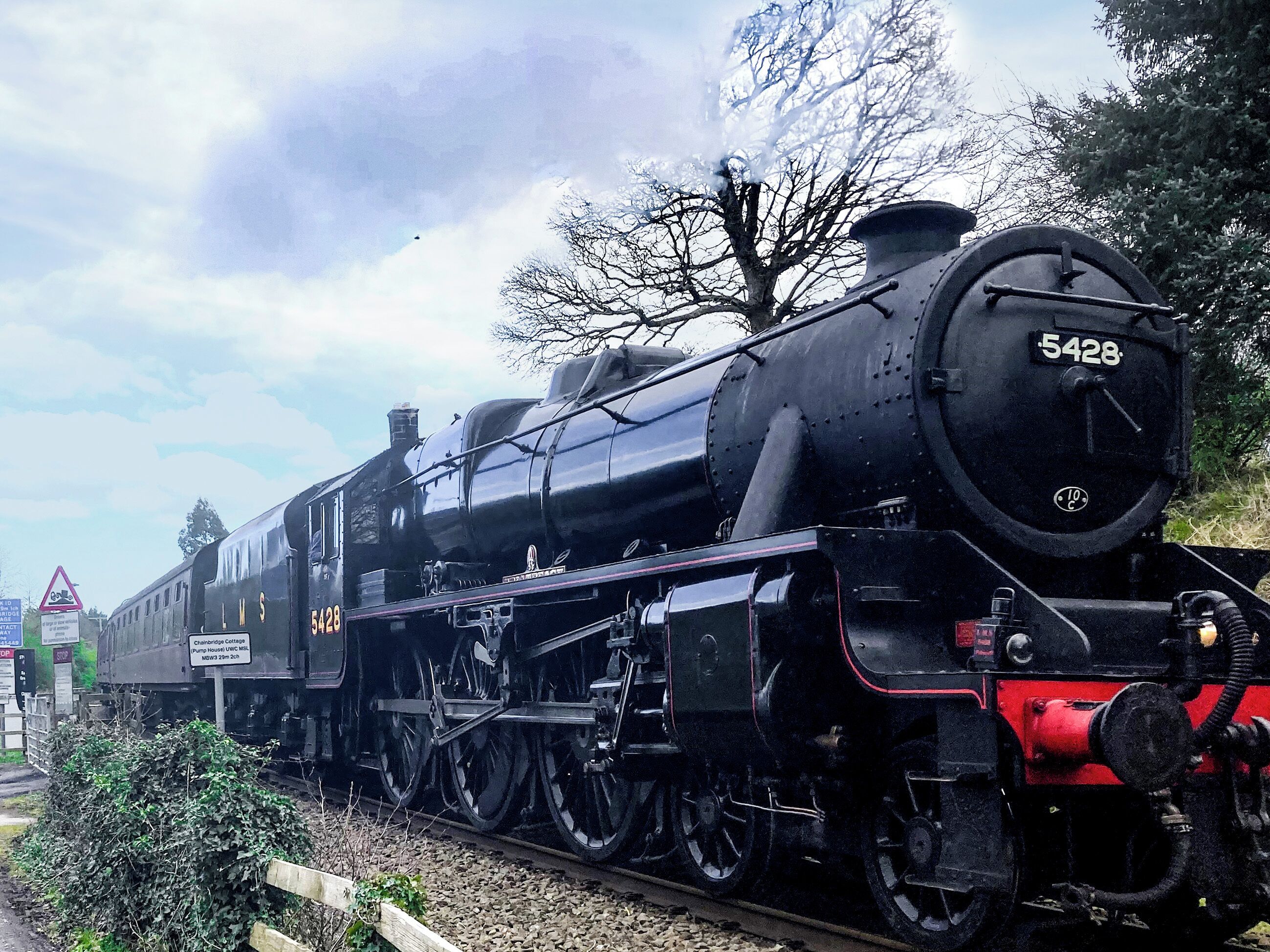 A black steam locomotive numbered 5428 on tracks with a sign indicating a pump house and a cottage.