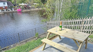A wooden picnic table with a bottle and glasses, near a river with a fence and greenery. - 2 bedroom accommodation in Ruswarp, near Whitby (Ruswarp, near Whitby)