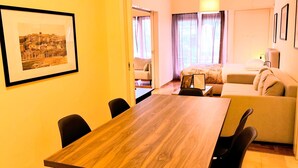 A hotel room with a wooden dining table, a sofa, a bed, and a framed picture on the wall. - Grand apartment in Acropolis museum (Athina)