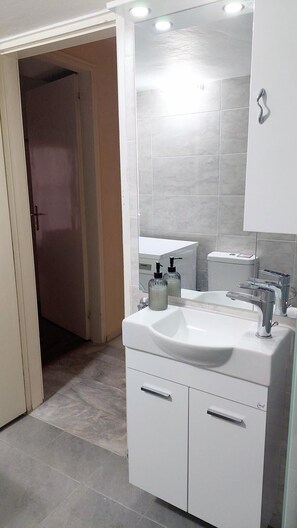 Ein modernes Badezimmer mit einem weißen Waschbecken, einem Spiegel und gefliesten Wänden.