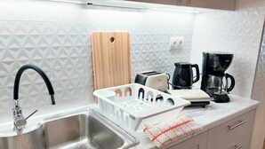 A kitchen with a stainless steel sink, a wooden cutting board, a toaster, a coffee maker, and a white dish rack. - Grand apartment in Acropolis museum (Athina)