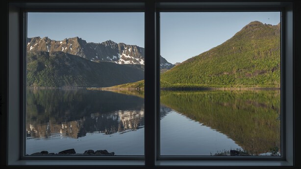 A room with two large windows offering a view of a lake and mountains. - Polar Panorama Lodge (Senja)