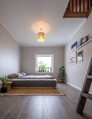 A bedroom with a bed, a window with plants, a wooden ladder, and a ceiling light. - Polar Panorama Lodge (Senja)