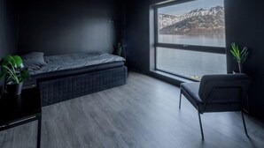 A modern bedroom with a large window, a bed, a chair, and a small table. - Polar Panorama Lodge (Senja)