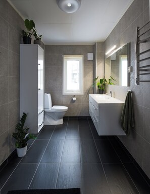 A modern bathroom with a toilet, sink, and large mirror. There are potted plants and a window providing natural light. - Polar Panorama Lodge (Senja)