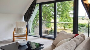 A modern living room with a black glass door leading to a garden, a white sofa, a wooden chair, and a black table with a bowl. - 1 bedroom accommodation in Aboyne (Aboyne)