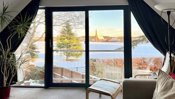 A living room with a sofa, a small table, and a view of a waterfront and trees through large glass doors. - 1 bedroom accommodation in Aboyne (Aboyne)
