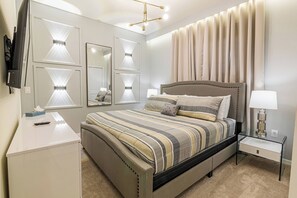 Een slaapkamer met een bed, nachtkastjes, een bureau en een aan de muur bevestigde televisie.