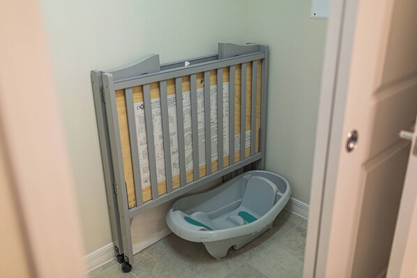 Babymand met een houten zijpaneel en een grijs frame, geplaatst tegen een wand in een badkamer.