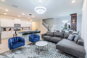 Una sala de estar moderna con un sofá gris, sillones azules y una mesa de centro blanca.