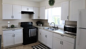 A modern kitchen with white cabinets, a black stove, stainless steel appliances, and a checkered floor mat.