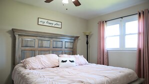 A bedroom with a bed, a ceiling fan, a window with curtains, and a wall sign.