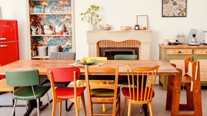 Een eethoek met een houten tafel, kleurrijke stoelen, een rode koelkast en een open haard met een bloemenornament.