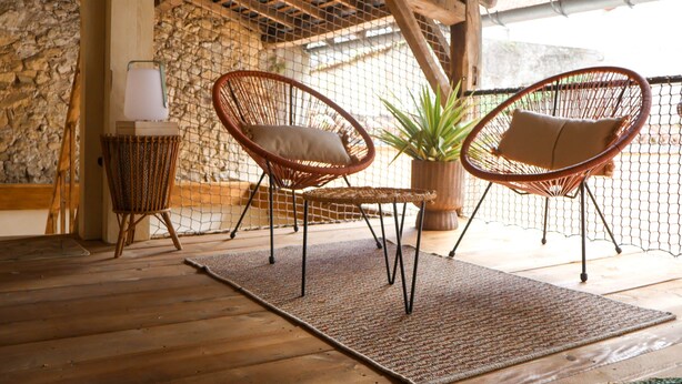 Een overdekt terras met rieten stoelen, een tafel en een lamp.
