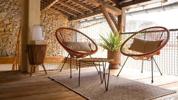 A covered outdoor seating area with wicker chairs, a table, and a lamp.