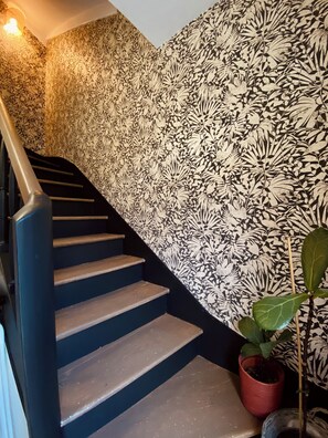 A staircase with a black handrail and steps, leading to a room with a floral wallpaper pattern. - Maison Malo Leone (Mauléon)