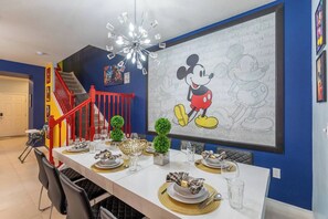 A dining area with a large Mickey Mouse mural, a chandelier, and a red staircase. - Marvelous Home Private With Pool and PS5 (Davenport)