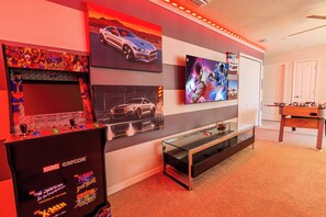 Een kamer met een gameconsole, wanddecoratie, een flatscreen-tv en een tafelvoetbaltafel.