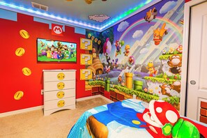 A child's bedroom with a Mario-themed mural, a television, and a bed with a Mario plush toy.