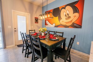 A dining area with a wooden table set for six, black chairs, and a Mickey Mouse painting on the wall.