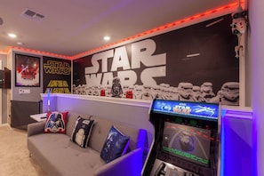 A Star Wars-themed room with a gaming console, Star Wars posters, and themed pillows.