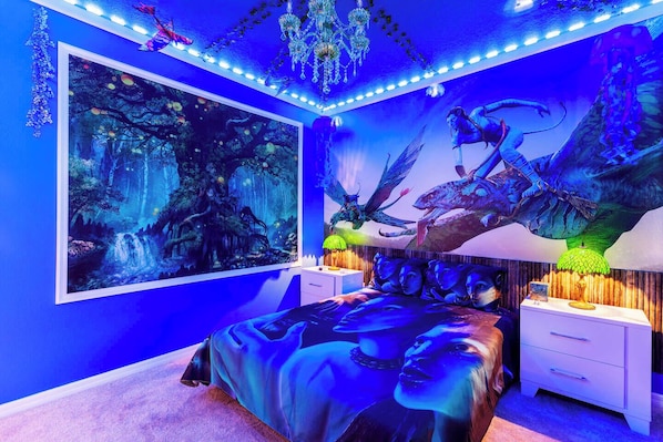 A bedroom with a large forest-themed mural, a bed with a dark blue bedspread, and a chandelier.